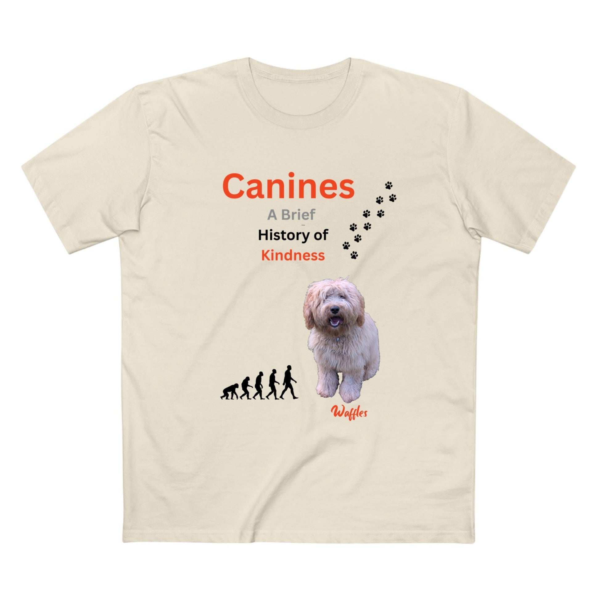 A beige short-sleeve t-shirt with a graphic print on the front. The print features the text 'Canines A Brief History of Kindness' in orange and black, a small black evolution sequence, a photo of a fluffy white dog, black paw prints, and the name 'Waffles' in orange script.